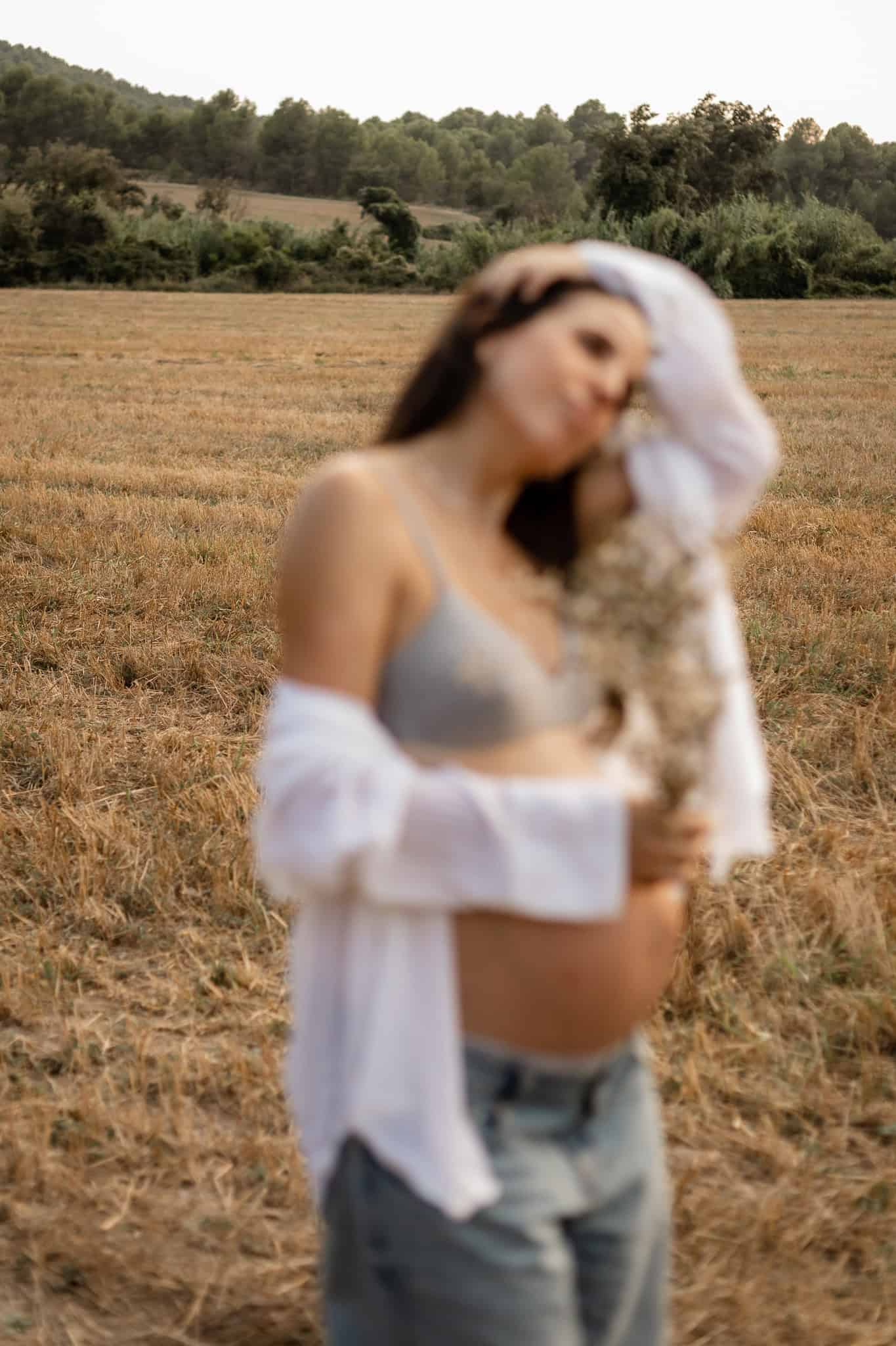 Mujer embarazada posa con gato en un campo rural al atardecer, estilo bohemio, natural y relajado, fotografía artística de maternidad y naturaleza.