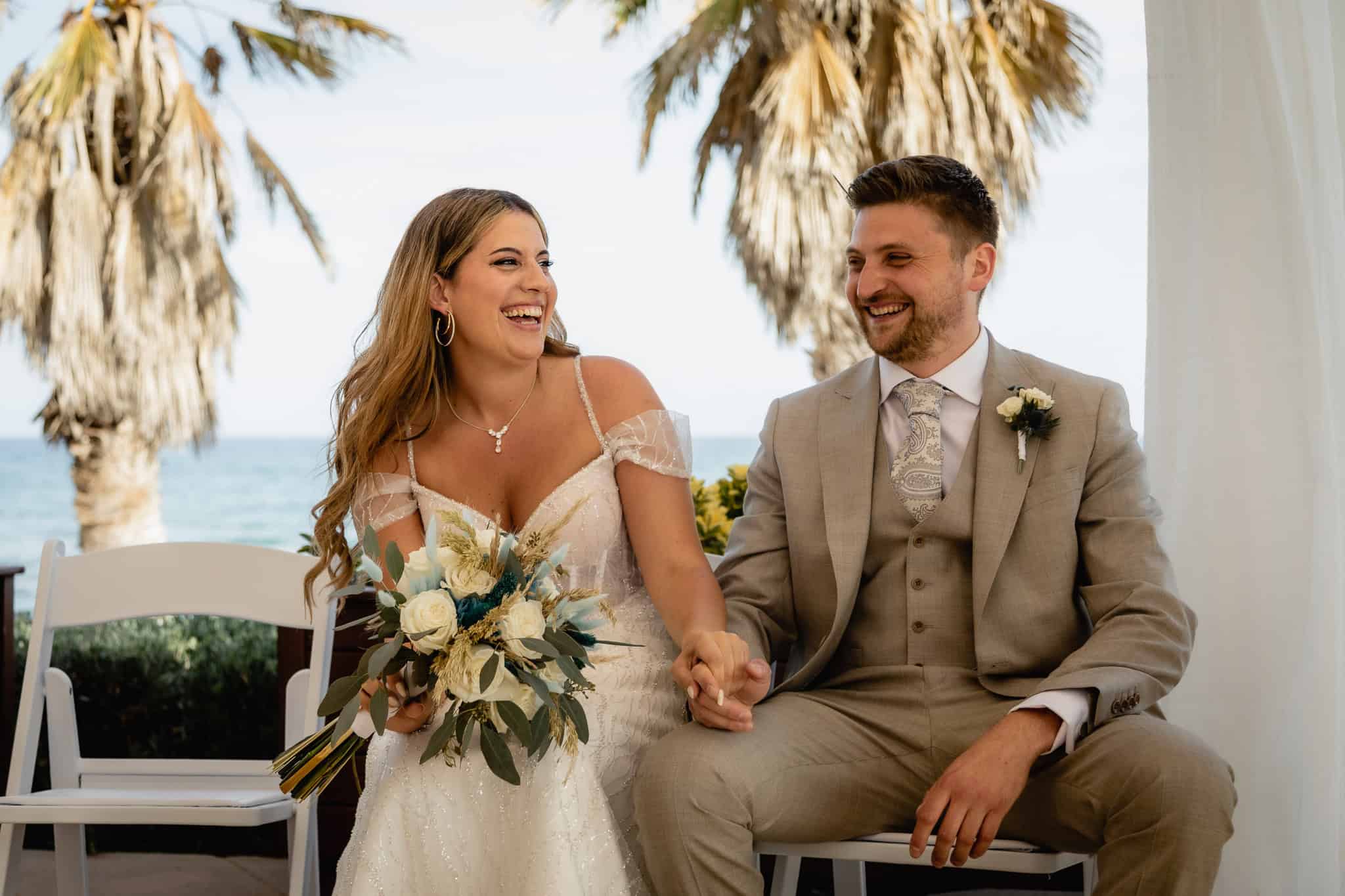 Sonrientes novios en boda al aire libre en la playa, luciendo elegantes trajes y vestidos de novia.